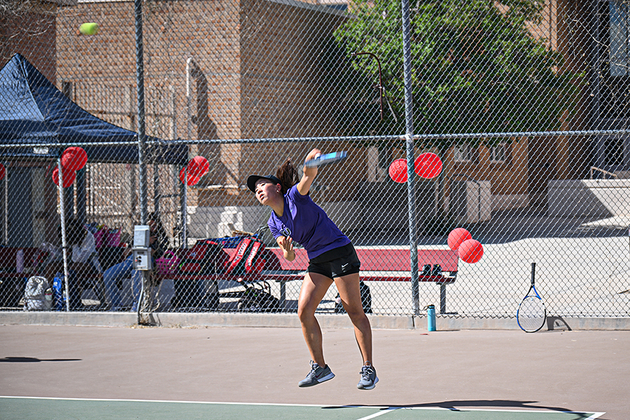 A girl swings the racquet hard to hit the tennis ball over the net