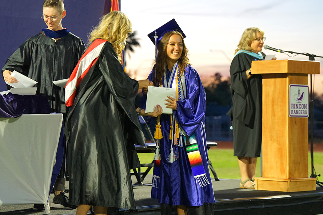 A graduate shakes a woman's hand as she accepts her diploma