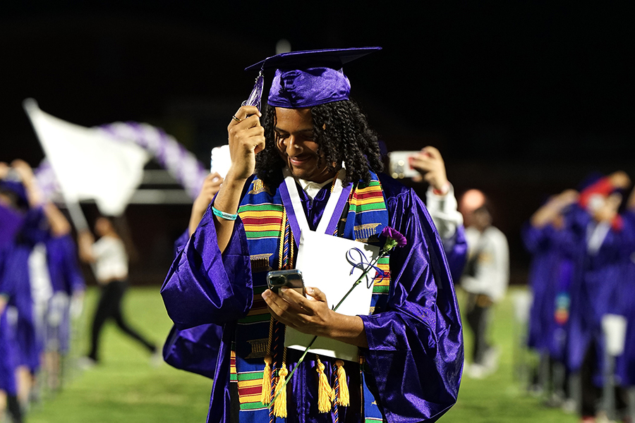 A graduate adjusts his tassel as he walks across the field