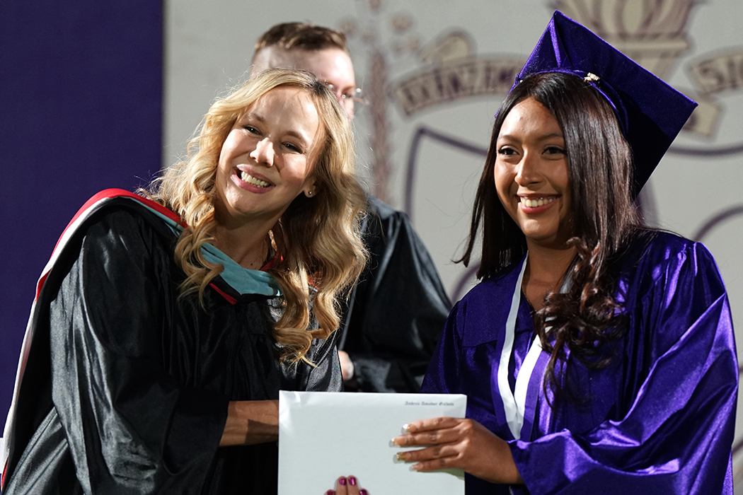A graduate shakes a woman's hand as she takes her diploma