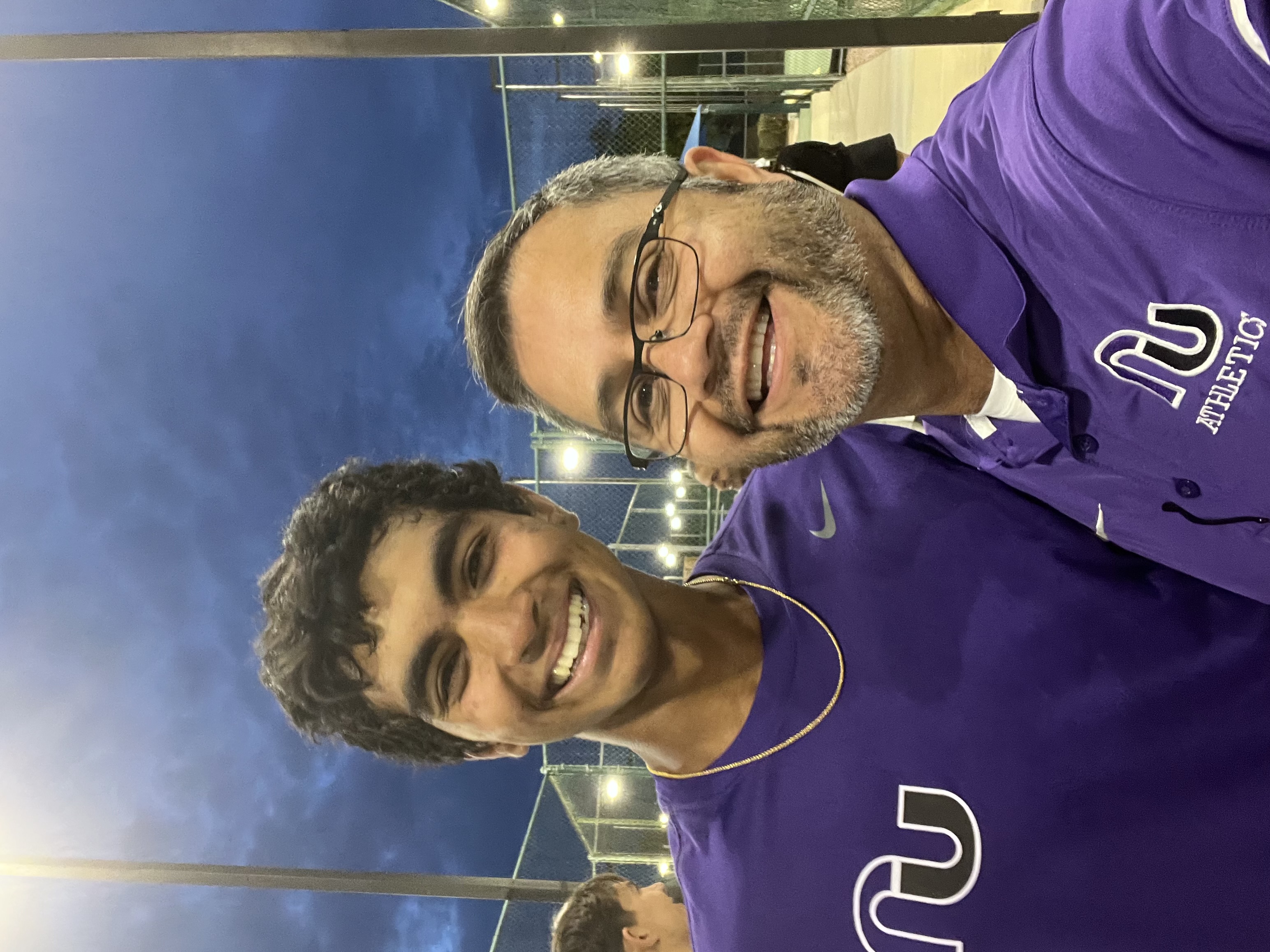 A teen boy and a man in glasses smile together on the tennis court