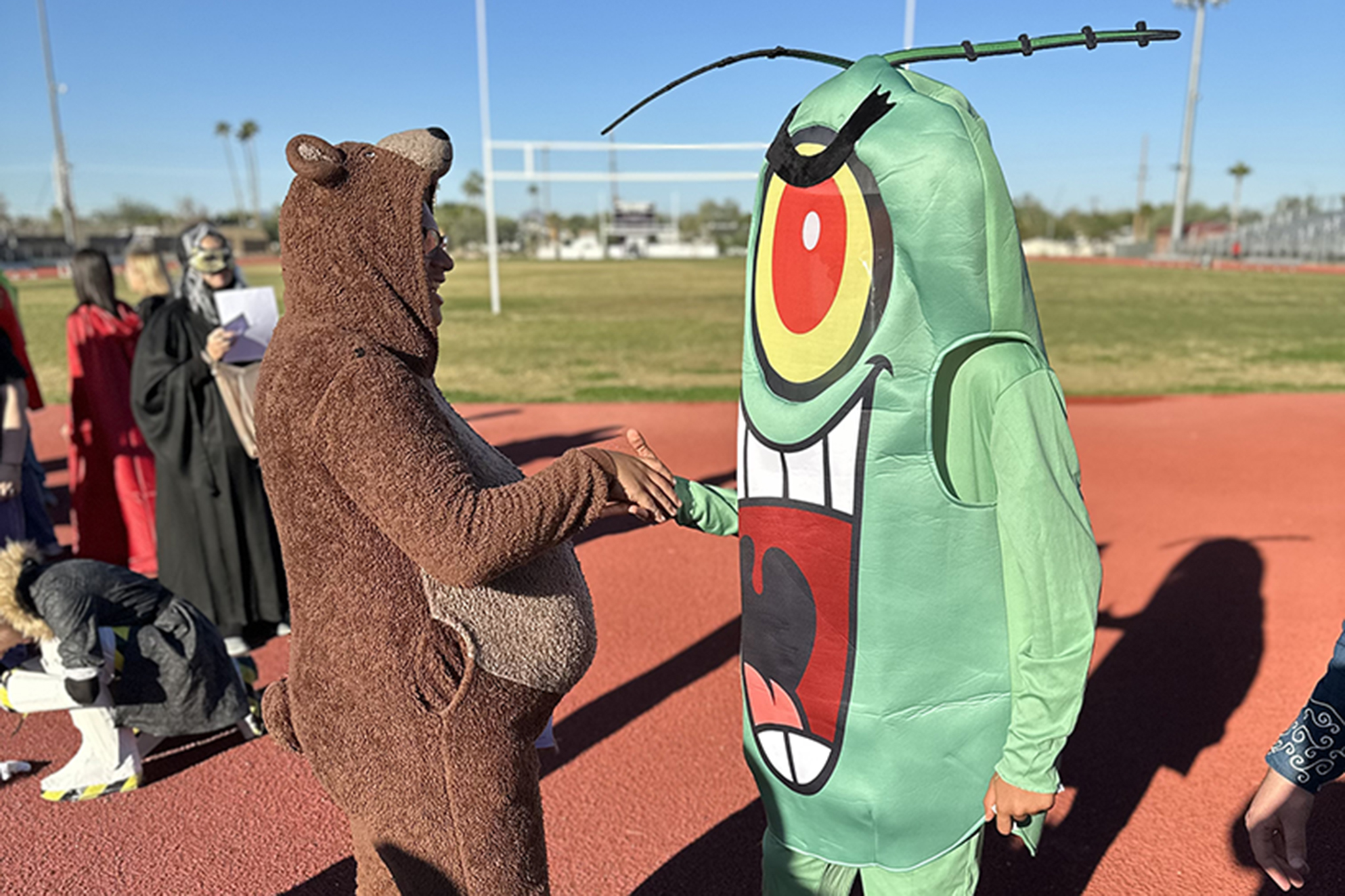 A person in a bear costume and a person in a green monster costume stand on the track