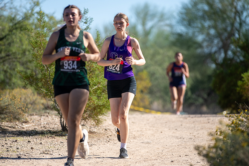 Three teen girls running on a dirt trail