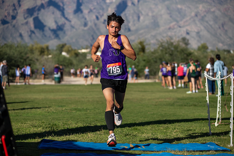 A teen boy runs across a grass field, with mountains in the background