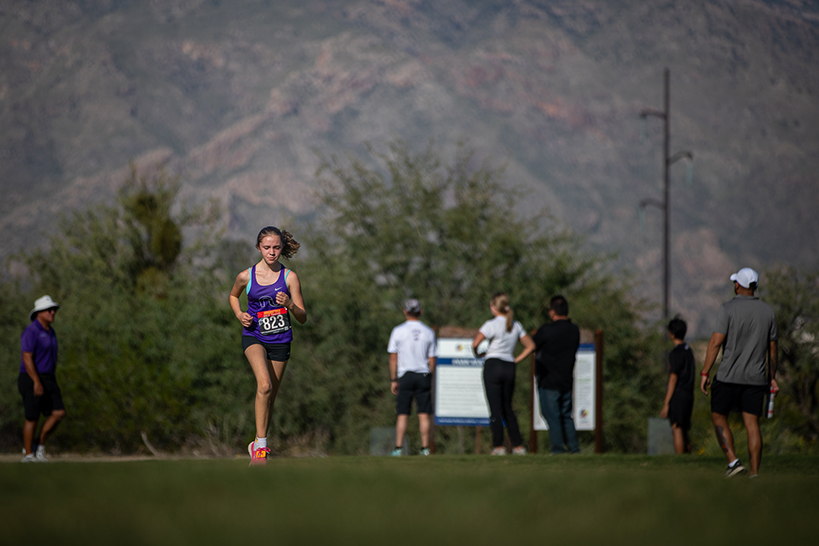 A teen girl runs across a grass field, with mountains behind her