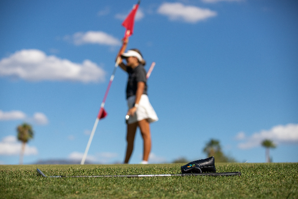 A teen girl leans on the golf flag, with a golf club in the foreground