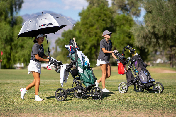 Two teen girls walk their golf caddies across the course