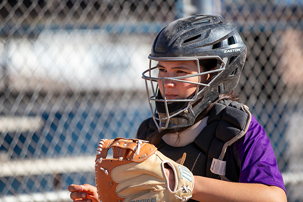 A girl in a catchers helmet waits for the ball
