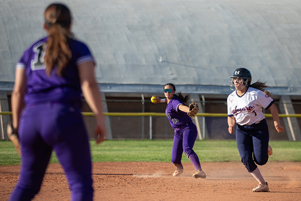 A girl tosses the softball to her teammate as an opponent runs by