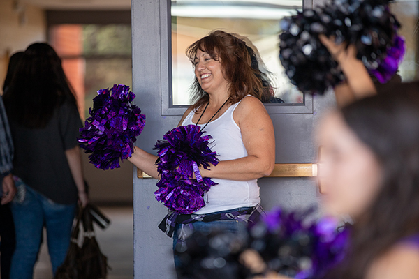 Women wave purple and black pompoms, welcoming families