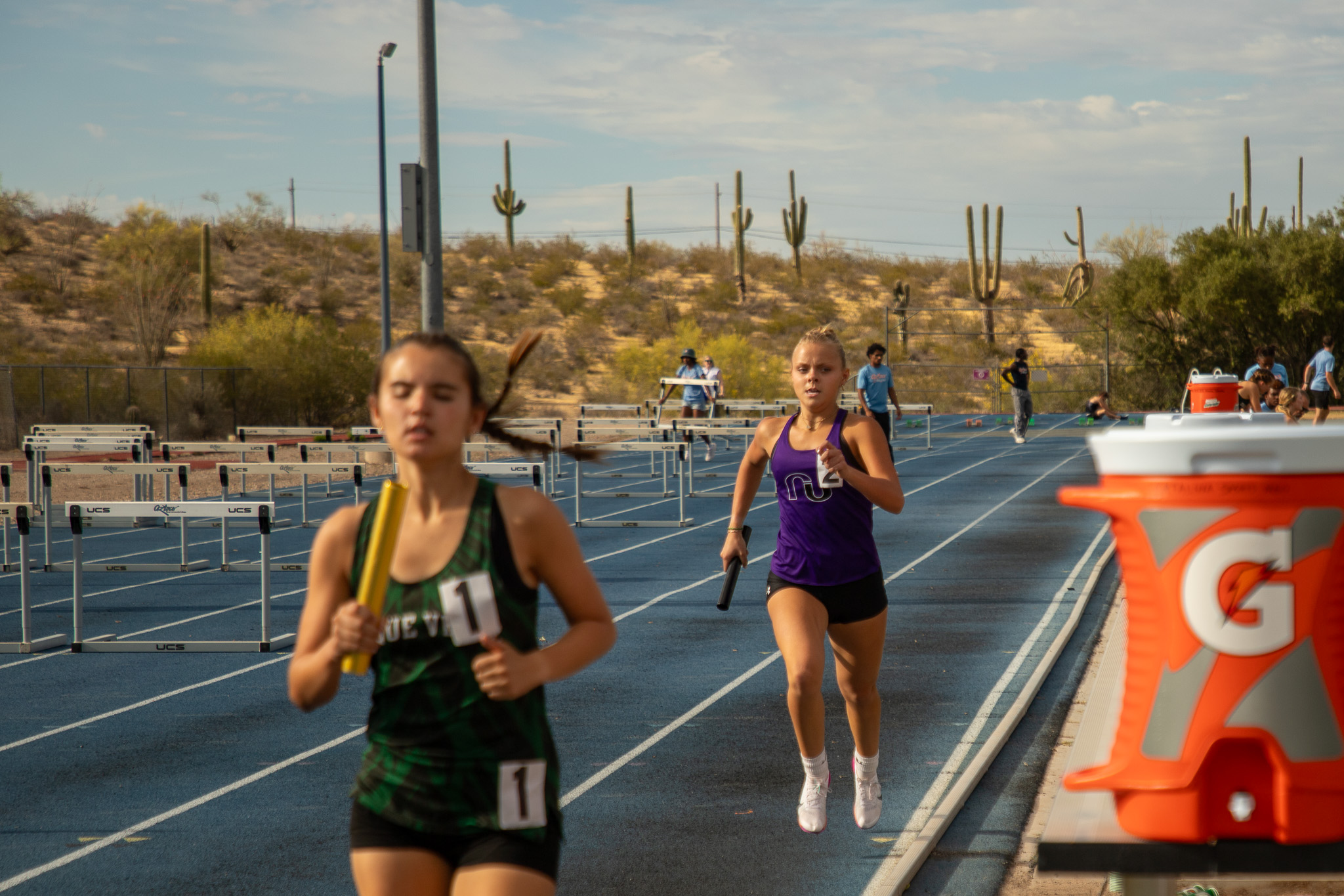Two girls run down the track holding batons during the relay