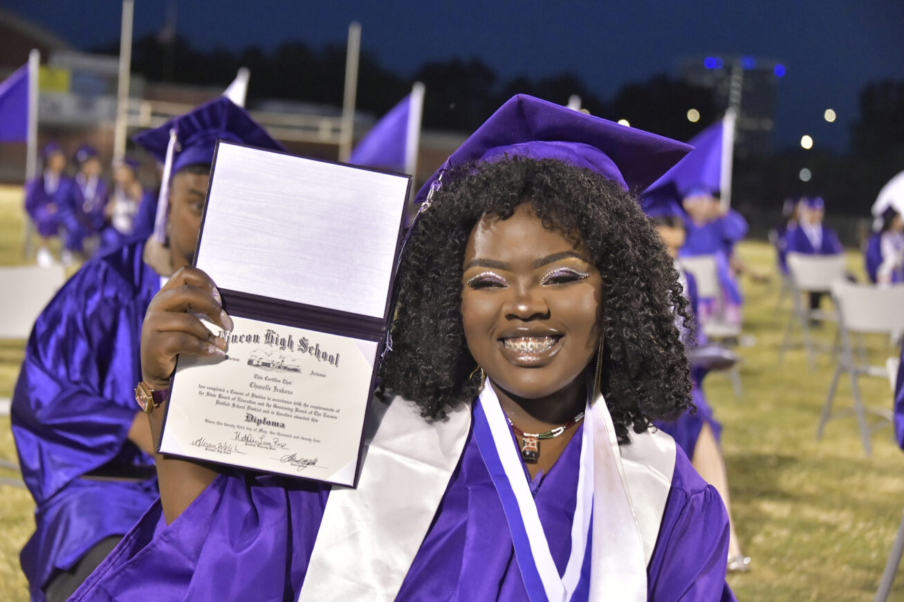 A smiling Rincon grad in her cap and gown holds up her diploma